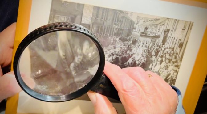 John looks at a black and white photograph of Gwydir Street residents celebrating VE Day through a magnifying glass.